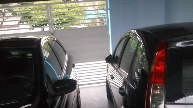 Dos coches estacionados en un área de estacionamiento techada, con piso de baldosas y pared azul.