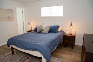 Een slaapkamer met een groot bed, twee nachtkastjes, een wandlamp en een raam met zonwering.