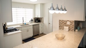 A modern kitchen with white cabinets, a built-in stove, a dishwasher, and a coffee maker. There are three pendant lights above the counter. - ☀️Casita bonita 🏖 Villa with 4beds/3 bath and HEATED pool 🌴🔥 (Sunrise)