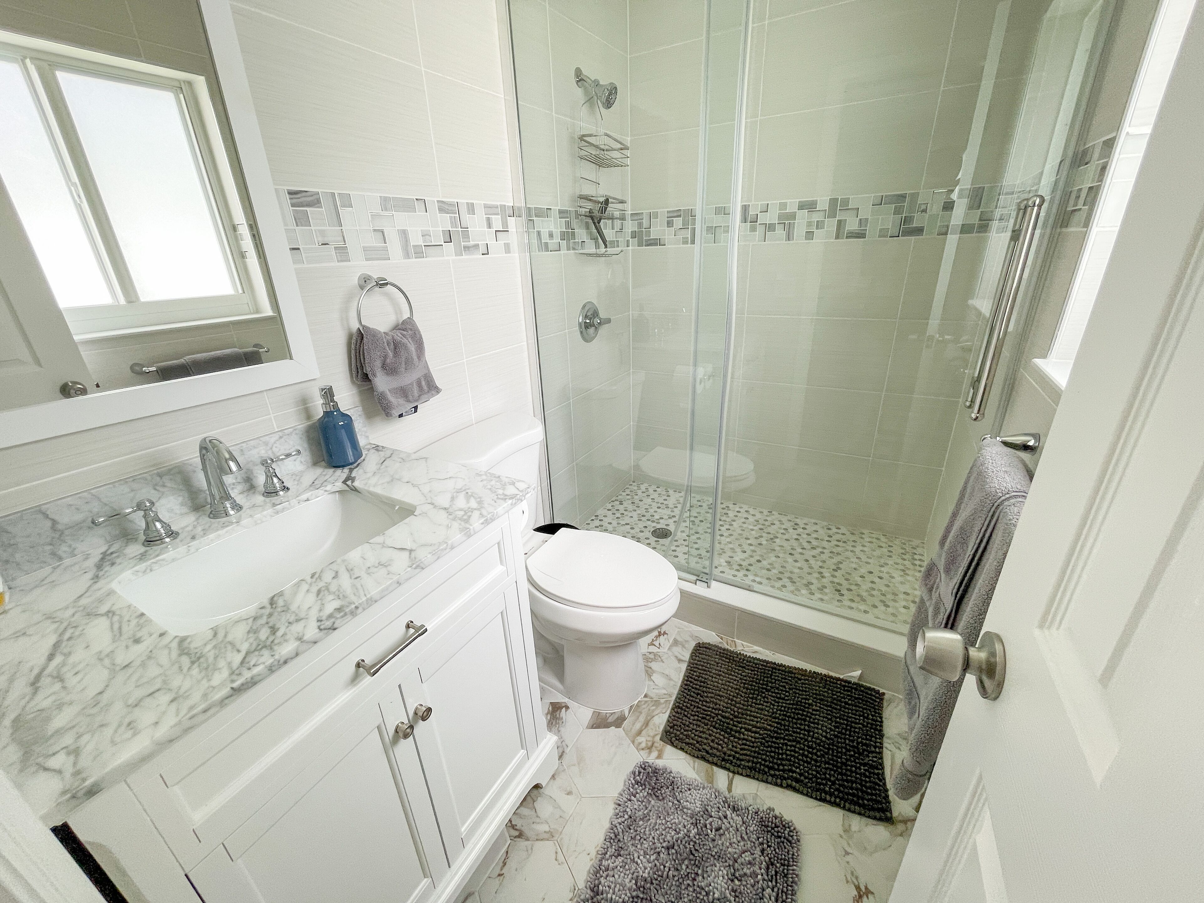 Une salle de bain avec une douche à parois de verre, des toilettes blanches, un lavabo en marbre et un miroir au-dessus du lavabo.