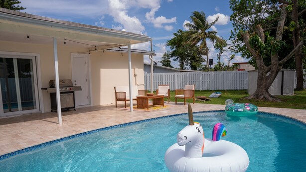 A swimming pool with a unicorn float, a covered patio area, and a backyard with a wooden deck and chairs. - ☀️Casita bonita 🏖 Villa with 4beds/3 bath and HEATED pool 🌴🔥 (Sunrise)