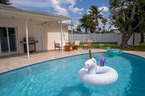 En pool med en uppblåsbar enhörning, en täckt uteplats och en trädgård med ett trädäck och stolar.