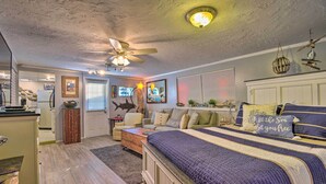 Ein Schlafzimmer mit einem großen Bett, einem Deckenventilator und Blick zur Küche.