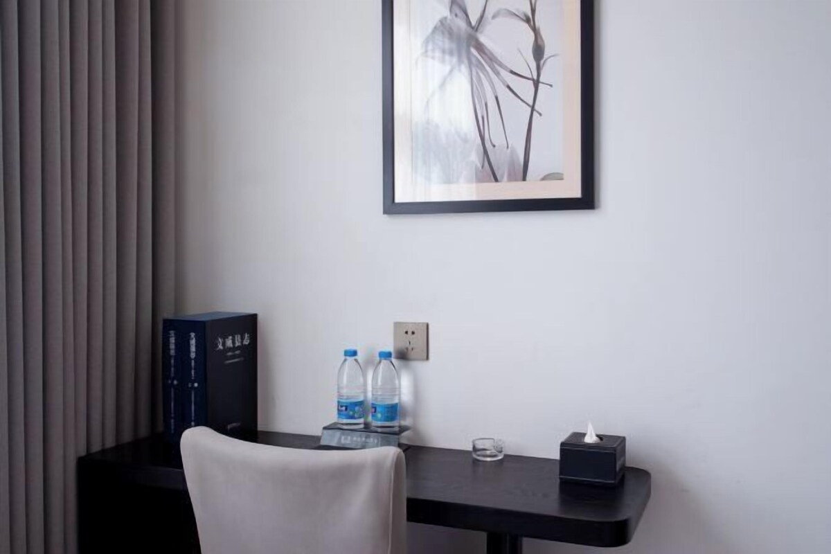 Habitación de hotel con escritorio, dos botellas de agua, caja de pañuelos y una obra de arte enmarcada en la pared.