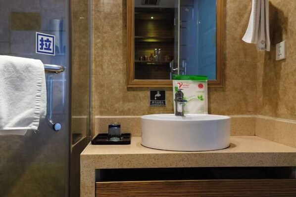Un baño con un lavamanos blanco, cabina de ducha de vidrio, perchero y un espejo.