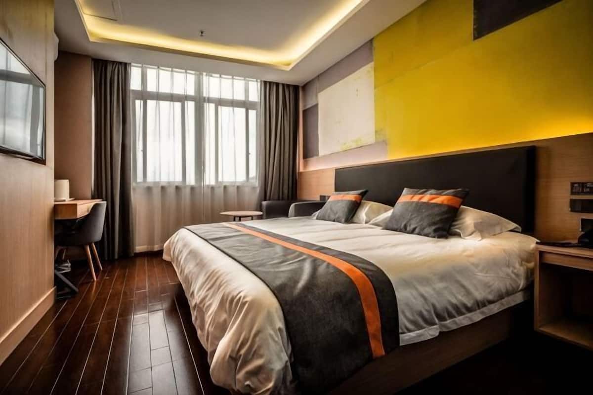 Una habitación de hotel con una cama grande, un escritorio y un ventanal con cortinas.