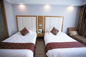 Habitación de hotel con dos camas, una mesita de noche, una silla y un cabecero de madera.