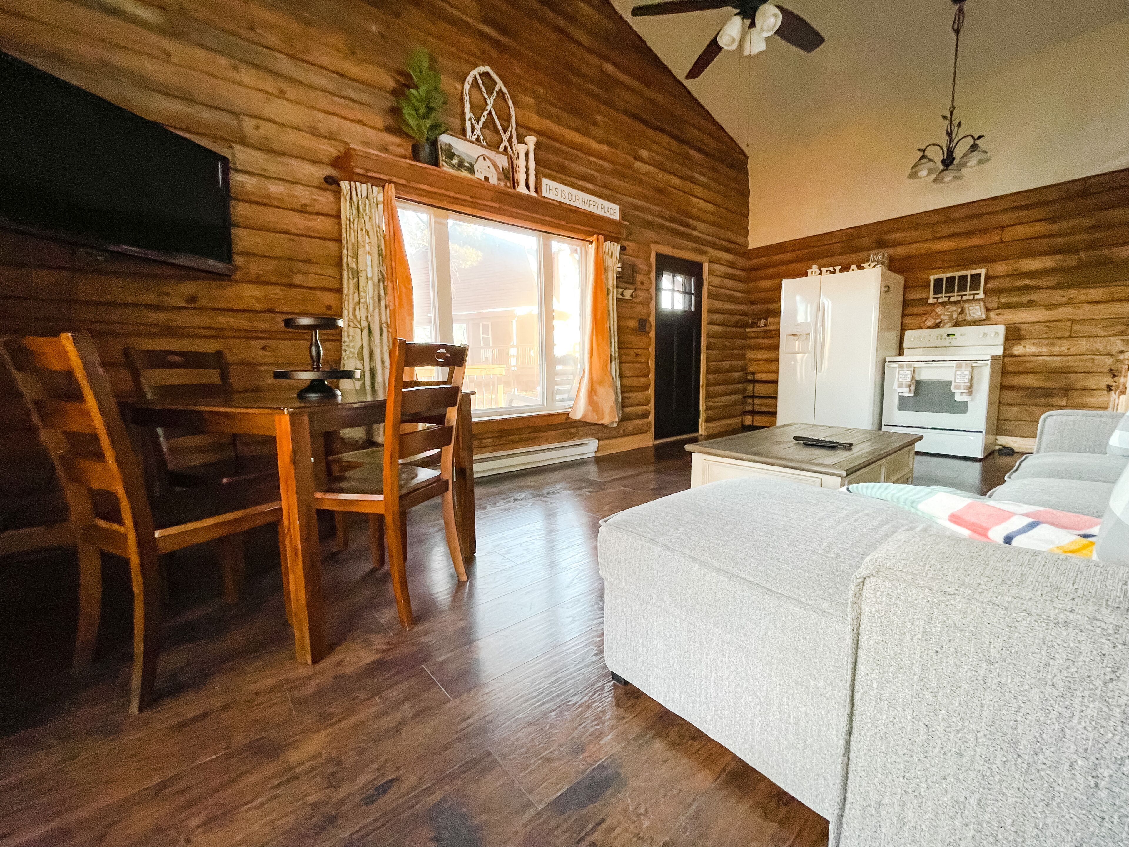 A cozy log cabin interior with a dining area, a sofa, a television, and a kitchen area.