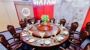 A round dining table with a central floral arrangement, surrounded by wooden chairs with cushioned seats. - Jintai Hotel (Tongguan)