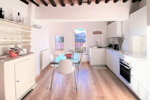 A modern kitchen with a dining area, wooden flooring, white cabinetry, and a view through an arched window. - CASA ILARIA - Bright apartment with a view in the historic center (Siena)