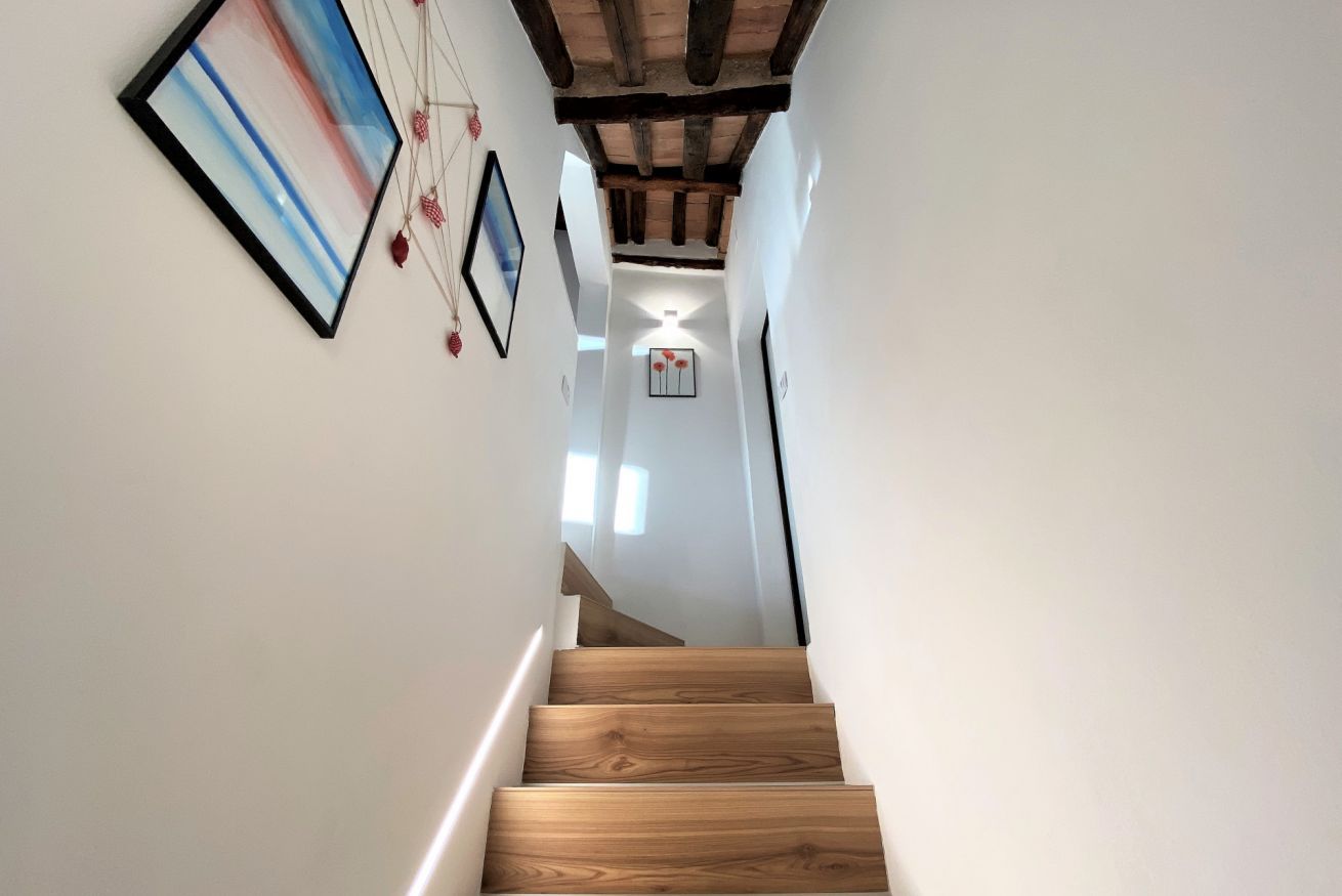 A wooden staircase leading to a room with white walls, framed artwork, and a ceiling with exposed beams.