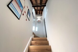 A wooden staircase leading to a room with white walls, framed artwork, and a ceiling with exposed beams. - CASA ILARIA - Bright apartment with a view in the historic center (Siena)