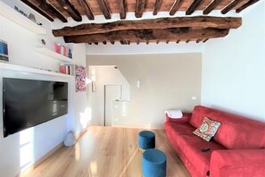 A living room with a flat-screen TV, red sofa, and blue ottomans. - CASA ILARIA - Bright apartment with a view in the historic center (Siena)