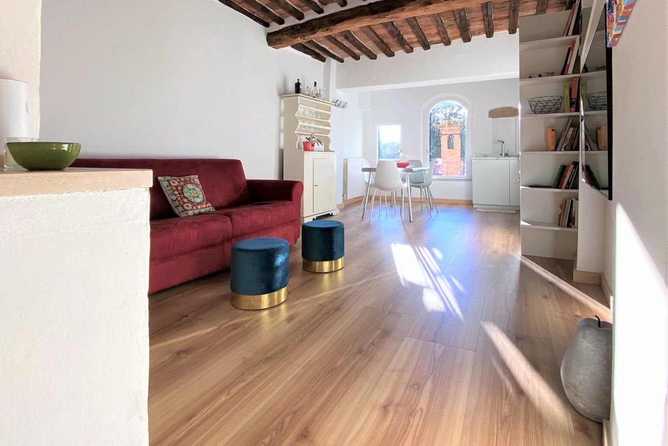 A modern living room with a red sofa, two blue ottomans, a wooden floor, and a bookshelf.