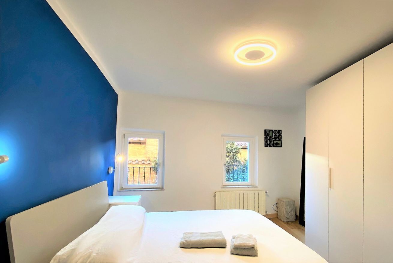 A bedroom with a bed, two windows, a radiator, and a wall-mounted light fixture.