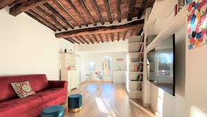 A modern living room with a red sofa, two ottomans, a TV, and a bookshelf. - CASA ILARIA - Bright apartment with a view in the historic center (Siena)