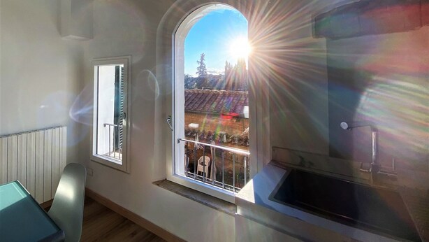 A room with a large window, a view of a balcony with outdoor furniture, and a kitchen area with a sink. - CASA ILARIA - Bright apartment with a view in the historic center (Siena)