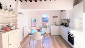 A modern kitchen with a dining area, wooden flooring, white cabinetry, and a view through an arched window. - CASA ILARIA - Bright apartment with a view in the historic center (Siena)