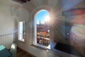 A room with a large window, a view of a balcony with outdoor furniture, and a kitchen area with a sink. - CASA ILARIA - Bright apartment with a view in the historic center (Siena)