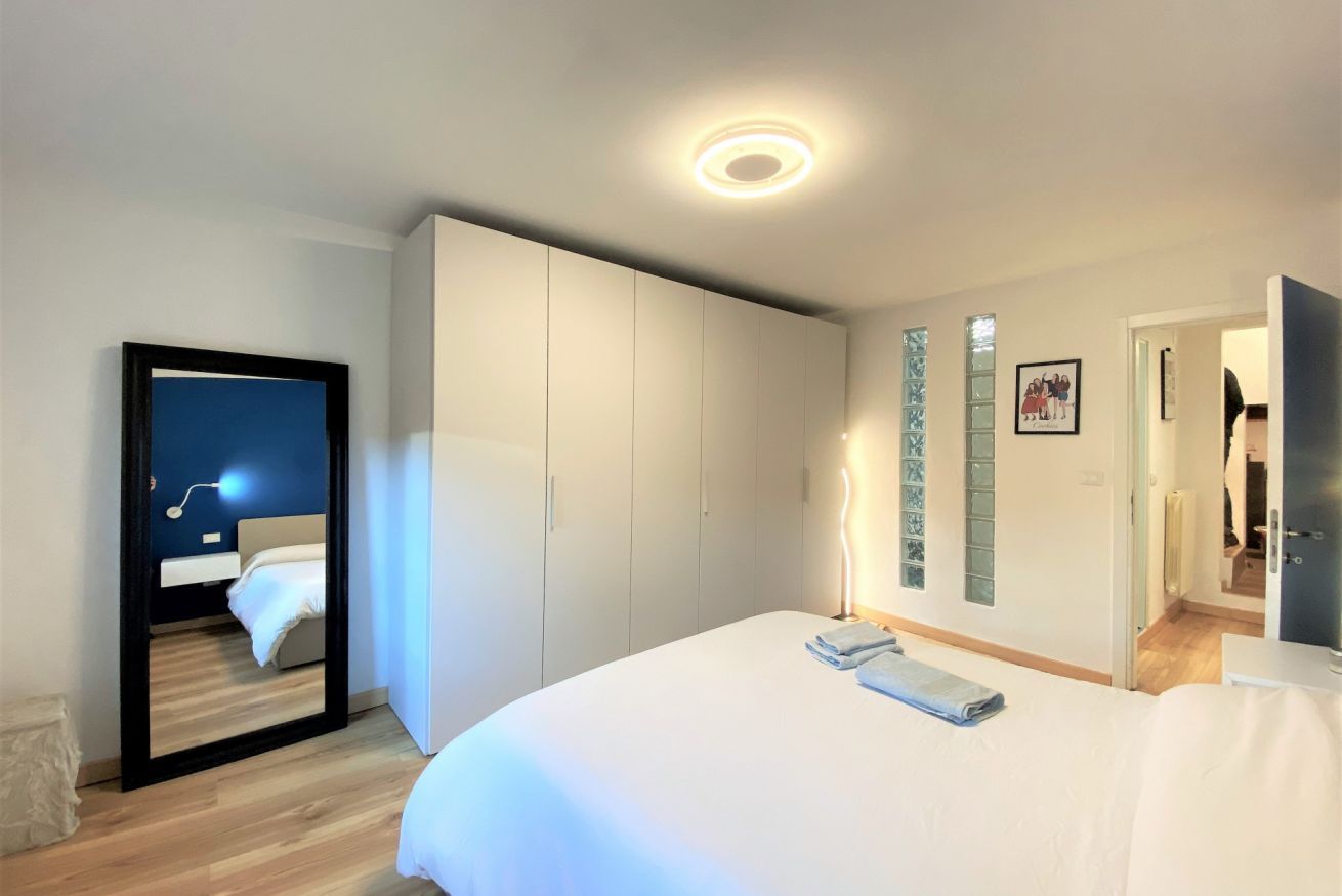 A modern hotel room with a large bed, a wardrobe, and a mirror reflecting a night scene.