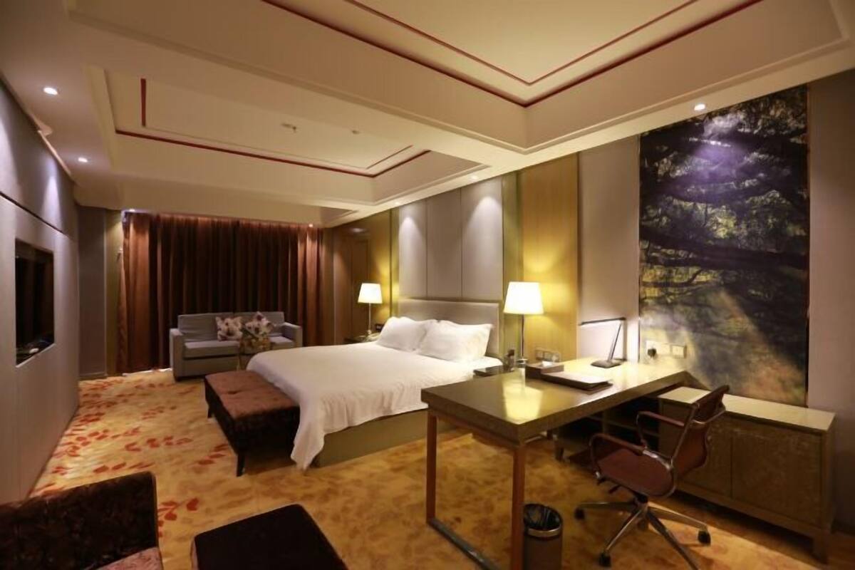 A hotel room with a bed, a desk, a chair, a sofa, and a large wall mural.