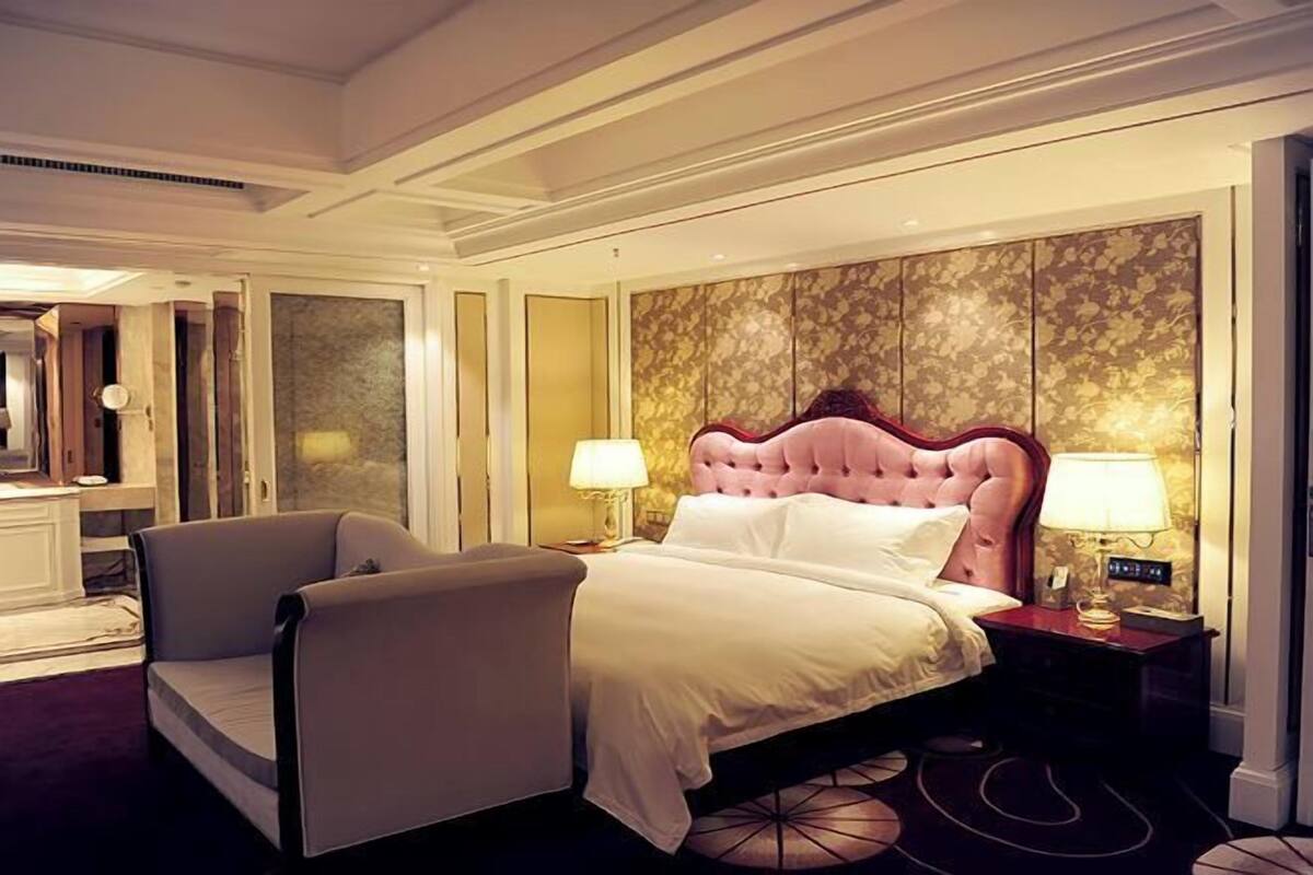 A hotel room with a large bed, two bedside tables, a chair, and a decorative wall panel.