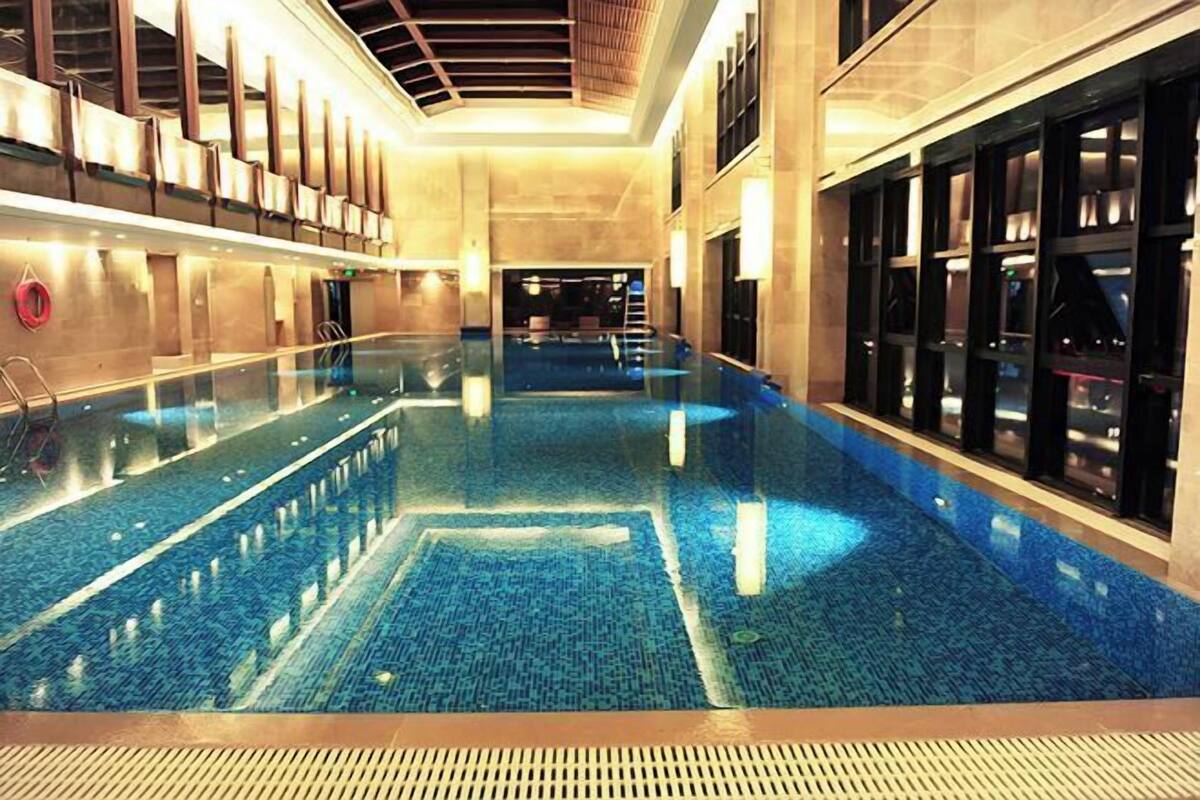 An indoor swimming pool with clear water, surrounded by walls with windows and a ceiling with a wooden design.