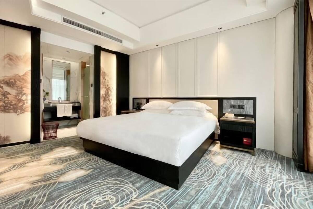 A modern hotel room with a large bed, a bedside table with a lamp, and a view of the bathroom.