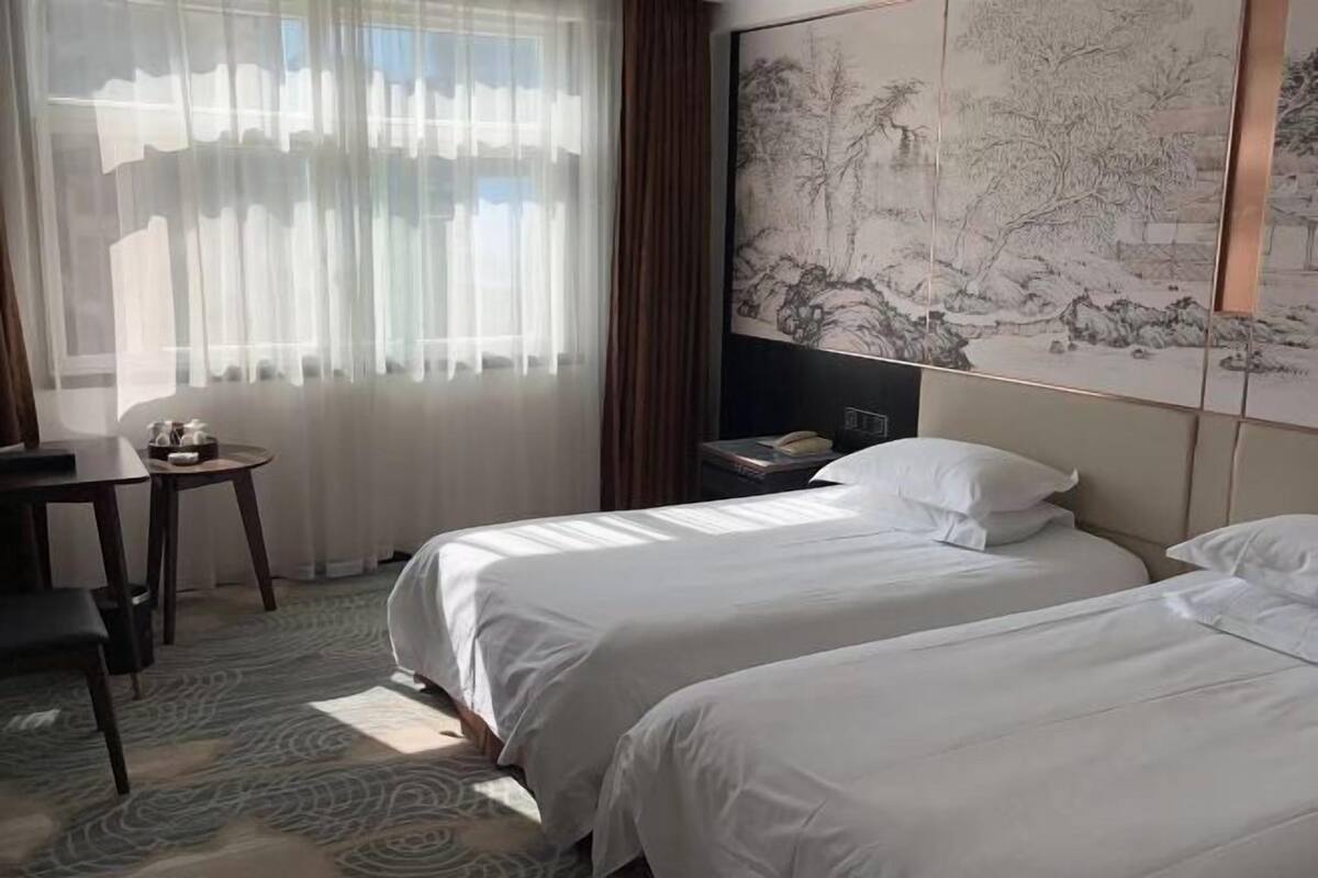 A hotel room with two beds, a desk, a chair, a nightstand, and a large wall painting.