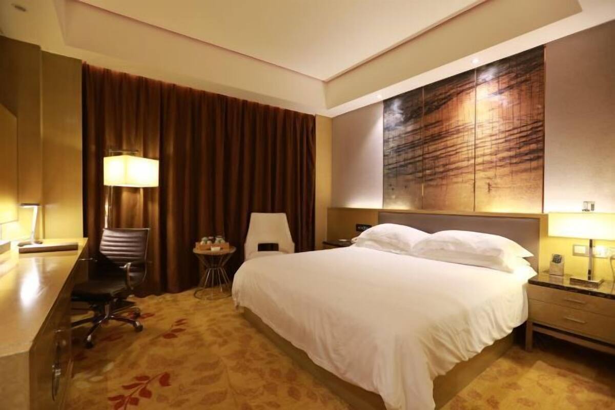 A hotel room with a bed, a desk, a chair, a lamp, and a wall with a textured design.