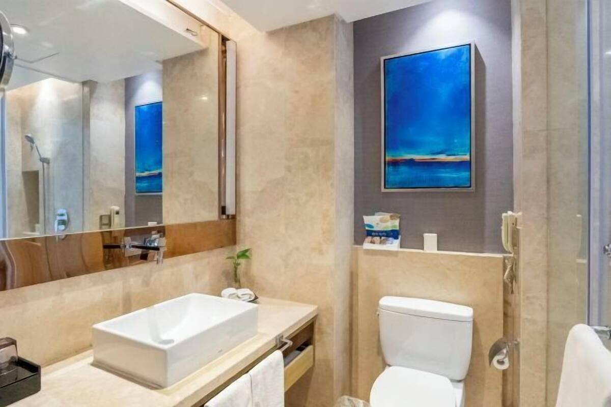 A modern bathroom with a large mirror, a white sink, a toilet, and a shower.