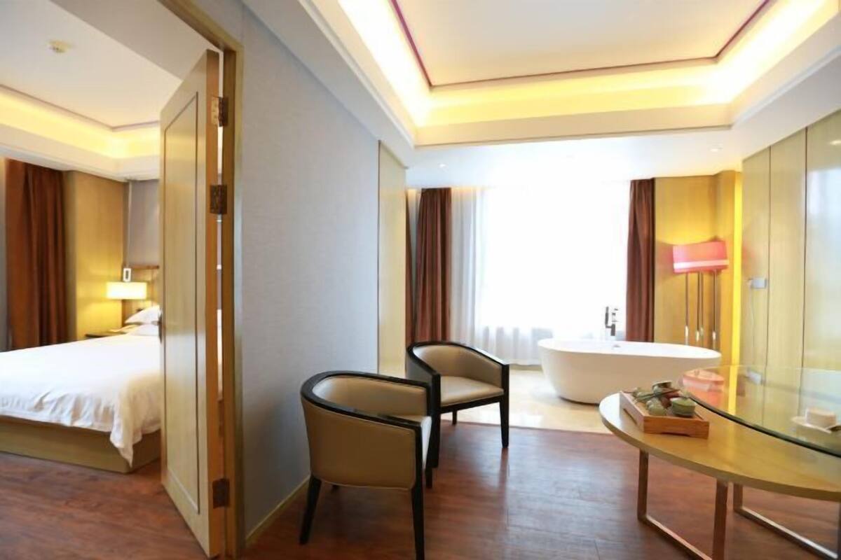 A hotel room with a bed, a chair, a glass table, a bathtub, and a large mirror.
