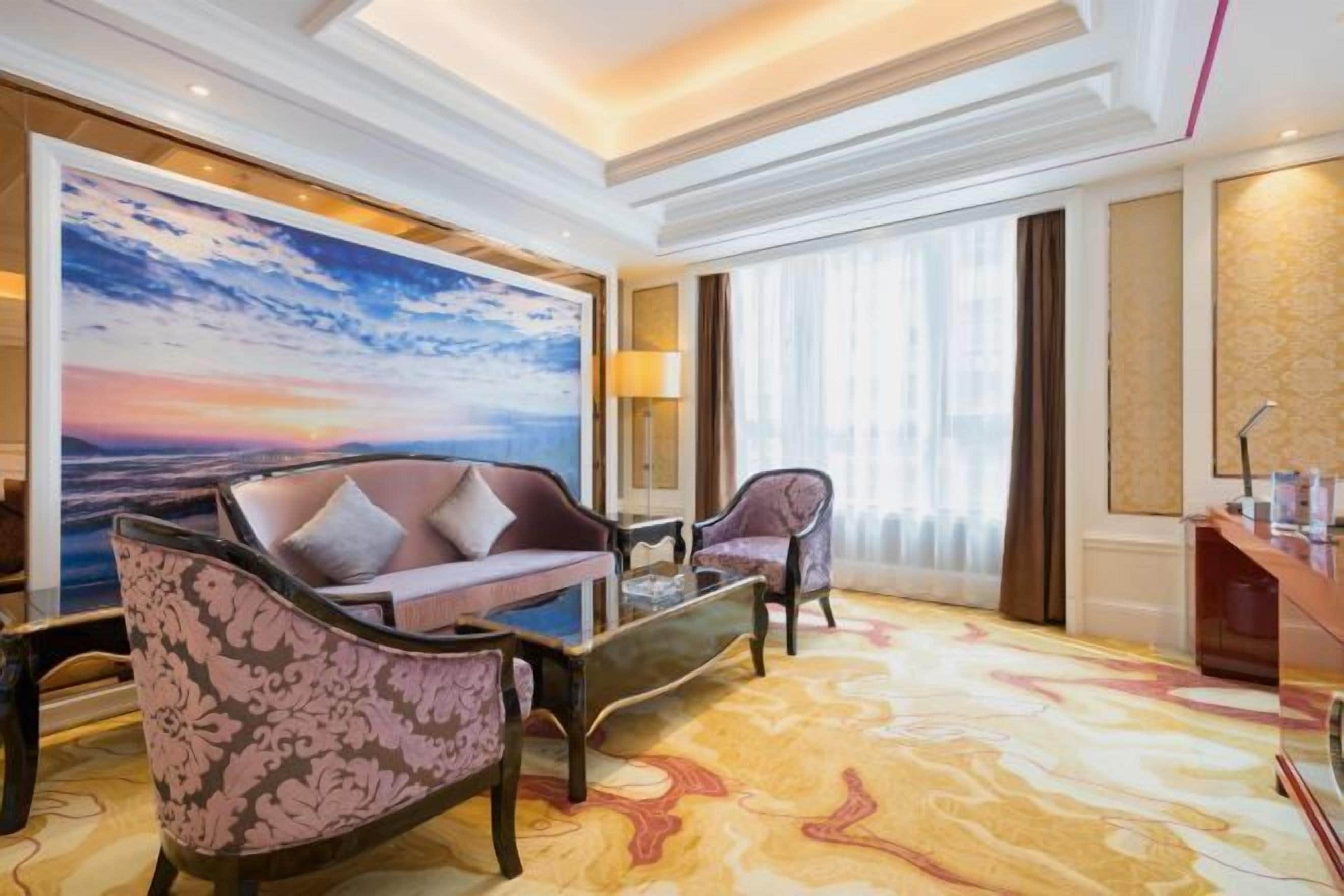 A spacious living room with a large painting of a sunset, a sofa, two armchairs, and a coffee table.