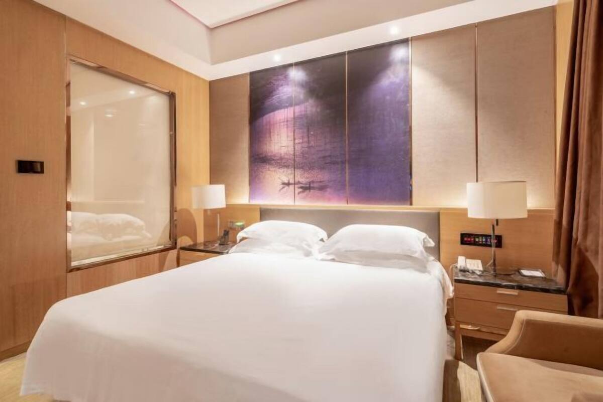 A hotel room with a large bed, a nightstand, a wall-mounted TV, and a window with curtains.