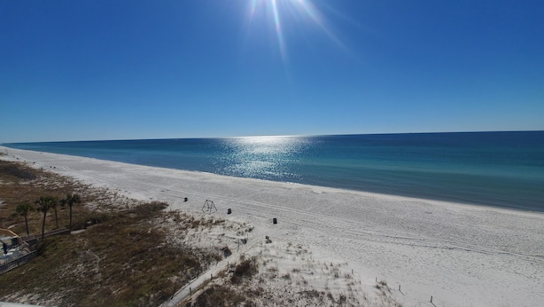 Uma praia com céu claro e o sol refletindo na água.