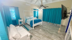 Quarto com cama de dossel, um sofá branco, uma TV e um ventilador de teto.