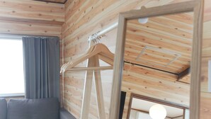 Ein Zimmer mit Holzwandverkleidung, einem grauen Sofa, einem Holzaufhänger und einer Deckenleuchte.