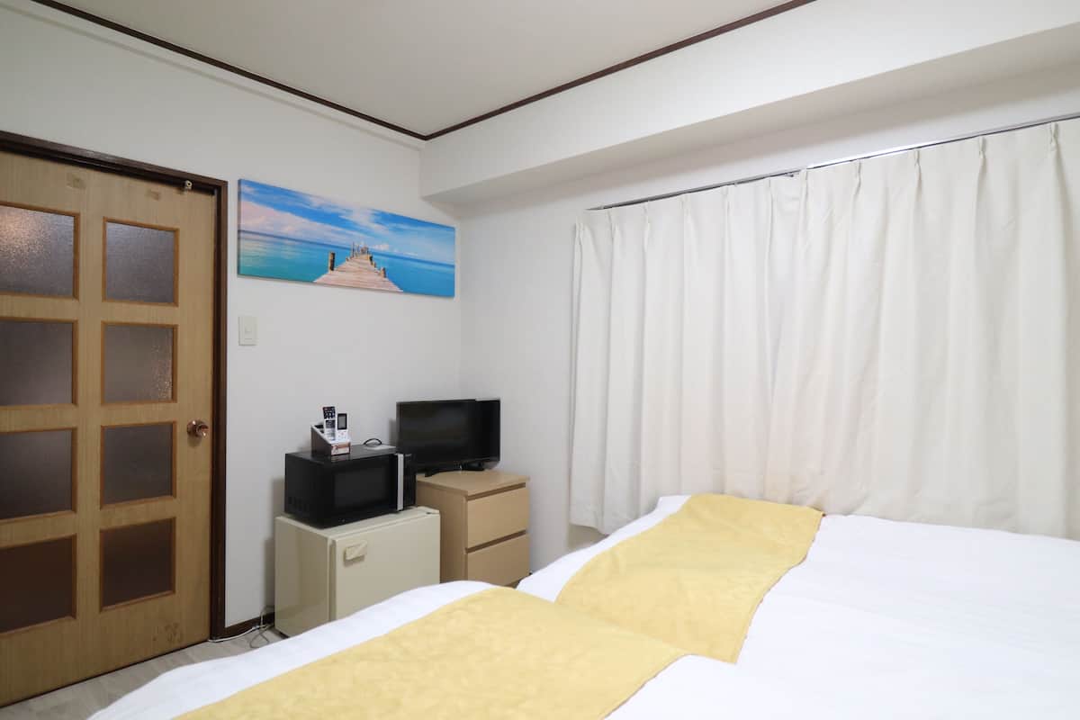 A hotel room with a bed, a television on a small cabinet, a door, and a painting on the wall.