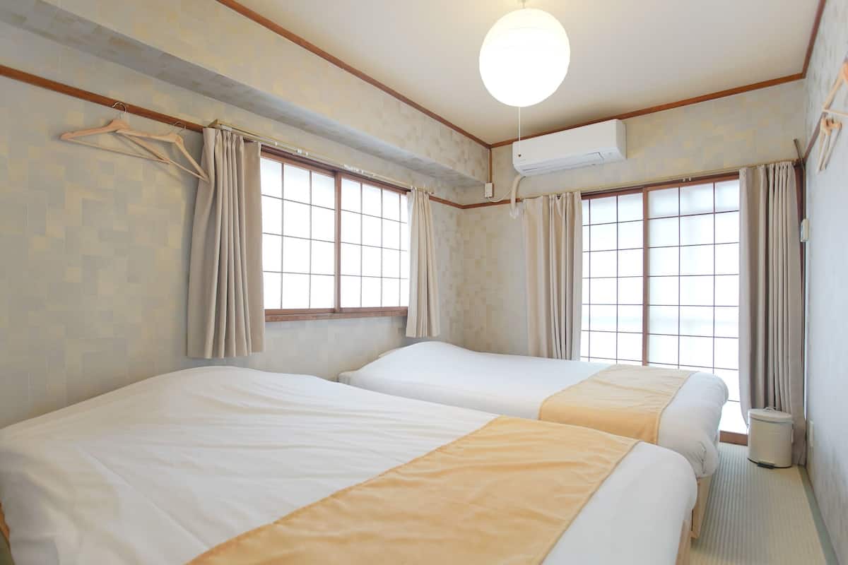 A hotel room with two beds, a window with curtains, an air conditioning unit, and a hanging coat rack.