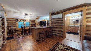 Interior de una cabaña de troncos con comedor, cocina y barra de madera.