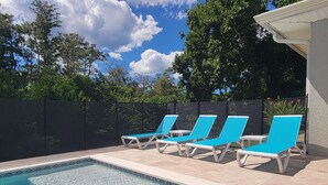 Une piscine avec quatre chaises longues bleues et une clôture noire.