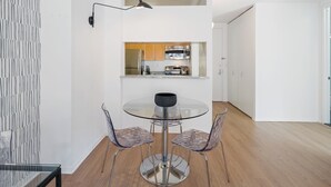 Ett modernt kök med vitvaror i rostfritt stål, ett matbord i glas och två genomskinliga stolar.