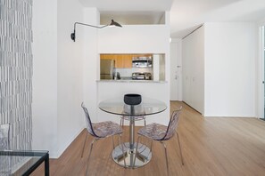Une cuisine moderne équipée d’appareils électroménagers en acier inoxydable, une table à manger en verre et deux chaises transparentes.