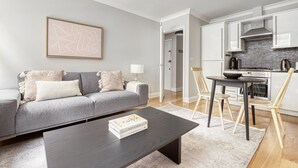 A modern living room with a grey sofa, a coffee table, and a dining area with a table and chairs. - Compact Covent Garden 2BR, 1 min to Embankment station, by Blueground (London)