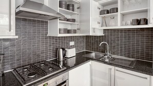 A modern kitchen with a gas stove, a built-in oven, a stainless steel sink, and white cabinetry. - Compact Covent Garden 2BR, 1 min to Embankment station, by Blueground (London)