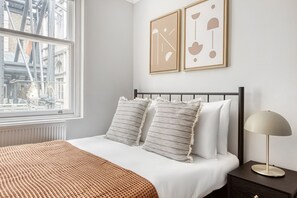 A neatly arranged bedroom with a bed, pillows, a bedside table, and a lamp. - Compact Covent Garden 2BR, 1 min to Embankment station, by Blueground (London)