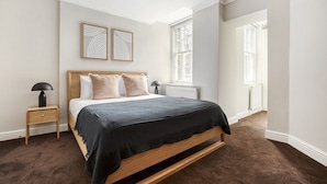 A bedroom with a wooden bed, two bedside tables, a radiator, and a window. - Compact Covent Garden 2BR, 1 min to Embankment station, by Blueground (London)