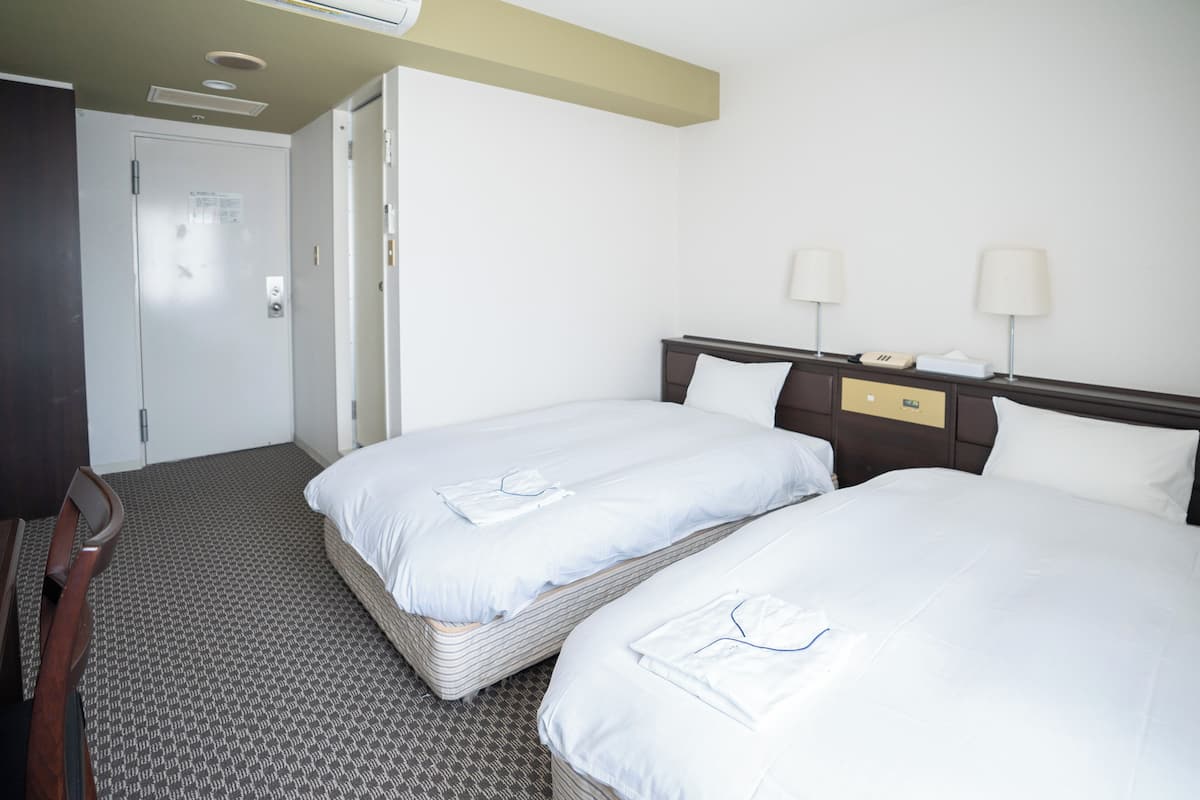 A hotel room with two beds, a desk, and a door.