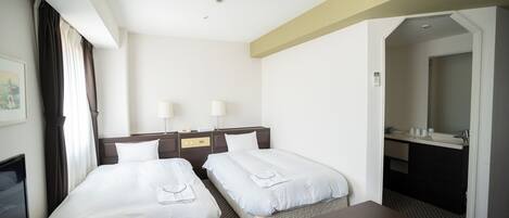 Habitación de hotel con dos camas, un escritorio, una silla, un televisor, un baño con lavamanos y espejo, y una alfombra estampada.
