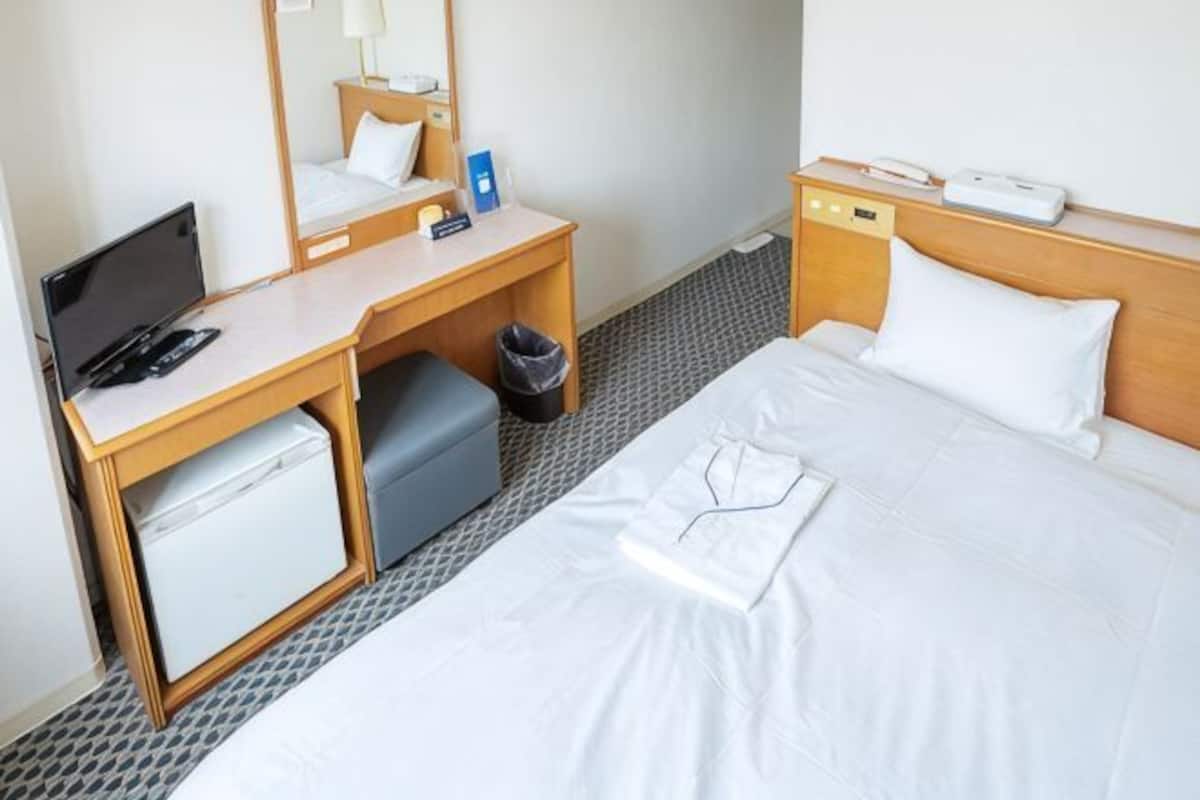 Une chambre dâhĂŽtel comprenant un lit, un bureau avec un ordinateur, un petit rĂ©frigĂ©rateur, une poubelle et une table de chevet avec un tĂ©lĂ©phone.